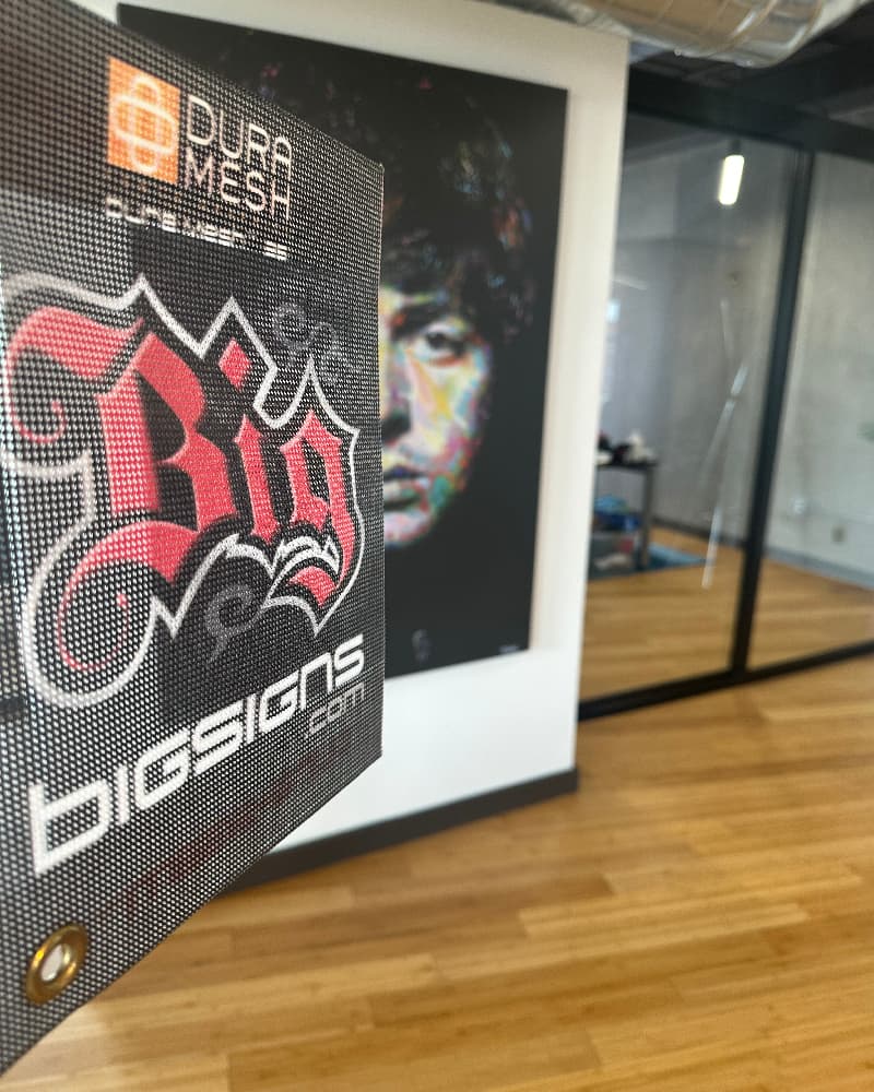 Duramesh mesh banner windscreen with sports-graphics hanging on chain-link fence for stadium or athletic facility.