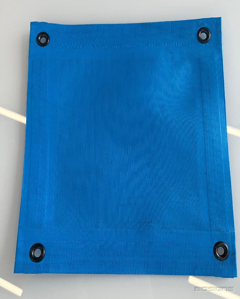 Blue mesh fence screen sample with sewn hems and a grommet in each corner