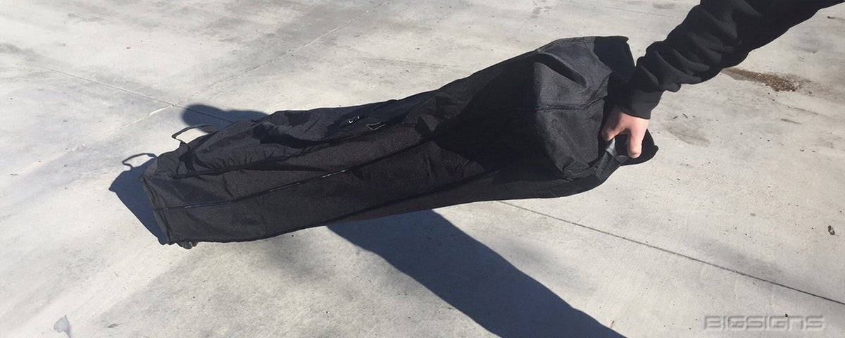 Person carrying a packed pop up tent in its black roller bag