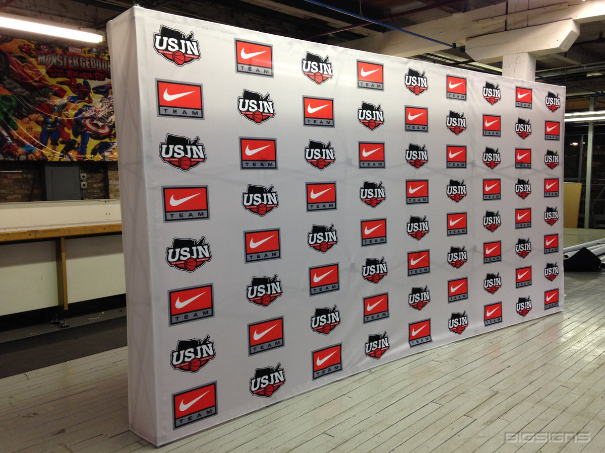 White USJN and Nike logo step and repeat pop-up backdrop in a warehouse