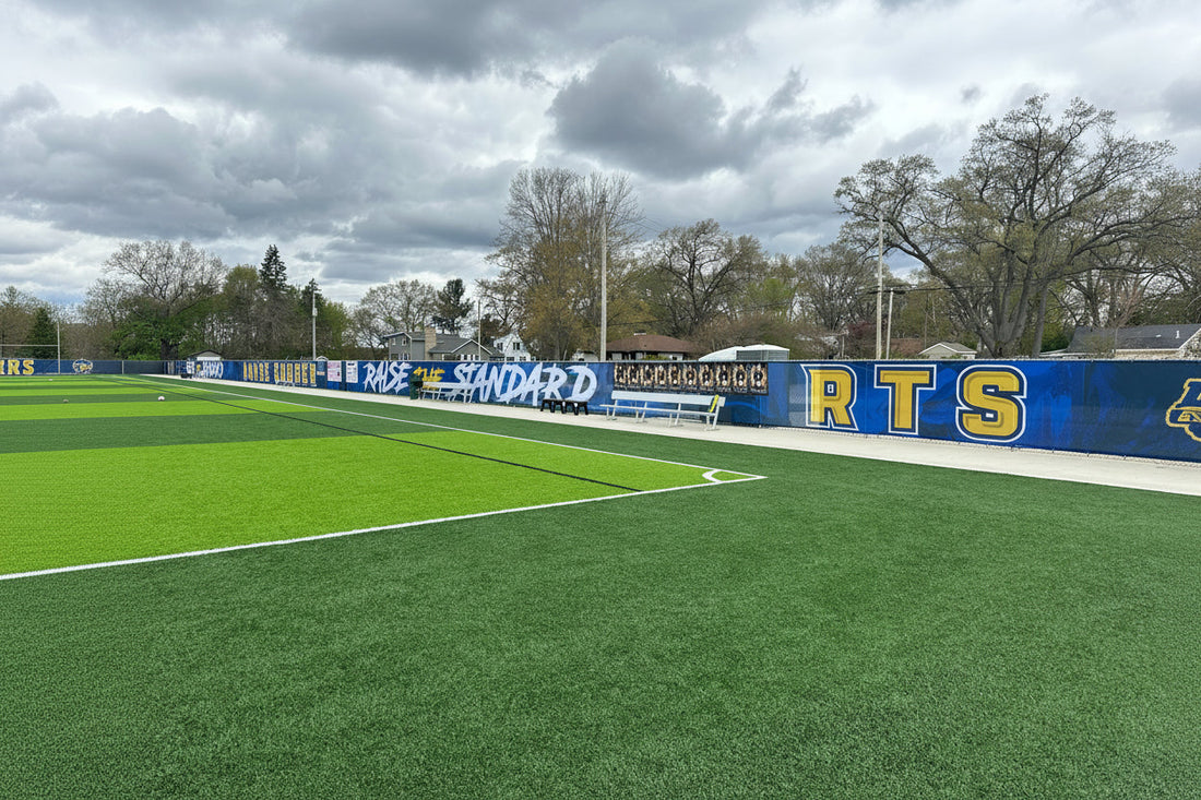 Black mesh athletic windscreen installed along a chain link fence at a school sports facility outfield perimeter