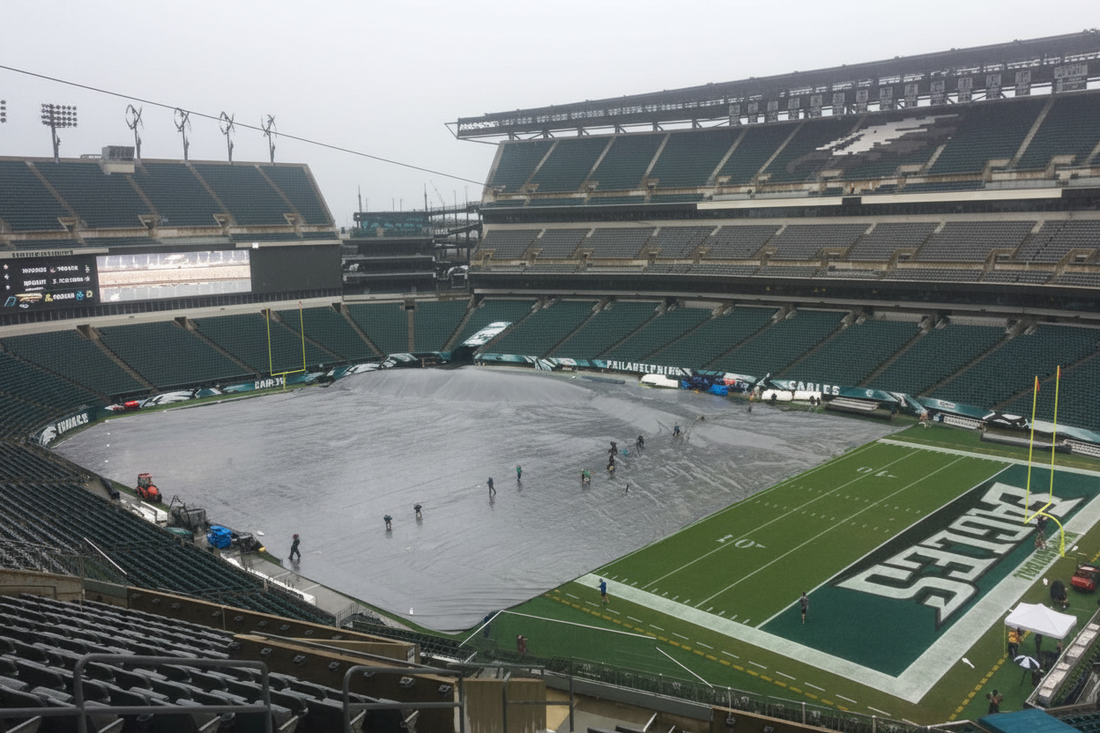 Grounds crew deploying a full-field rain tarp to protect the playing surface from rain at an NFL football stadium