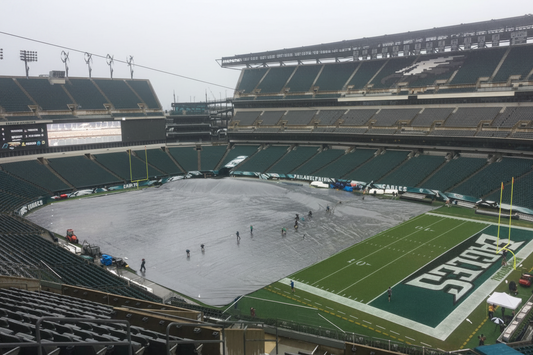 Grounds crew deploying a full-field rain tarp to protect the playing surface from rain at an NFL football stadium
