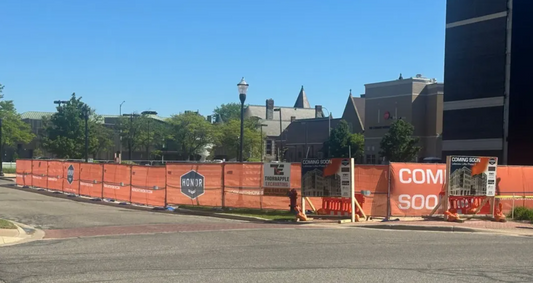 Orange printed mesh construction fence screen with branded signage wrapped around a downtown development site perimeter