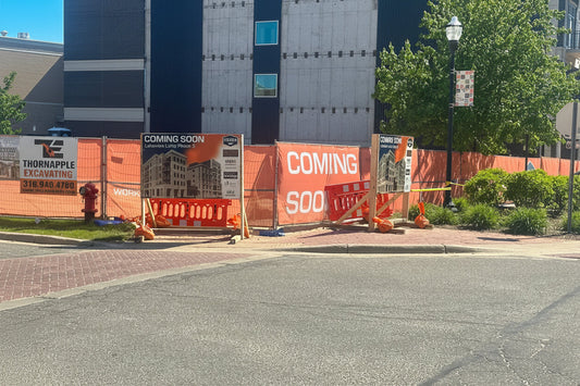 Orange printed construction fence screen showing Coming Soon leasing signage and contractor recognition graphics