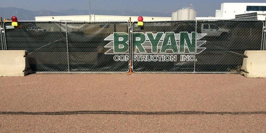 A construction fence screen with logo displaying “Bryan Construction Inc.” attached to a chain-link barrier at the jobsite.
