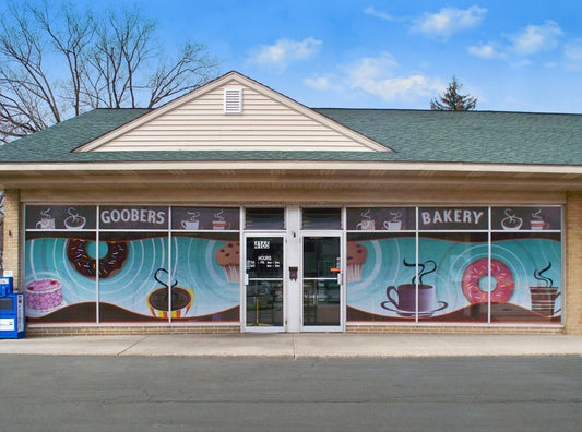 Bakery storefront featuring colorful window graphics with donuts, coffee cups, and muffins promoting Goobers Bakery.