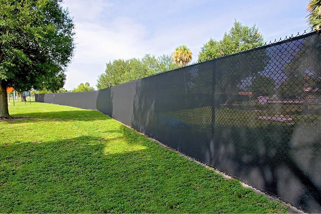 Black mesh fence screen installed on a chain link fence, providing outdoor privacy and wind reduction for open grassy areas