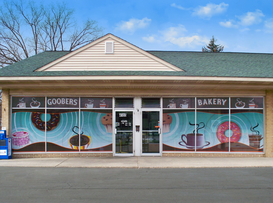 Bakery storefront featuring colorful window graphics with donuts, coffee cups, and muffins promoting Goobers Bakery.