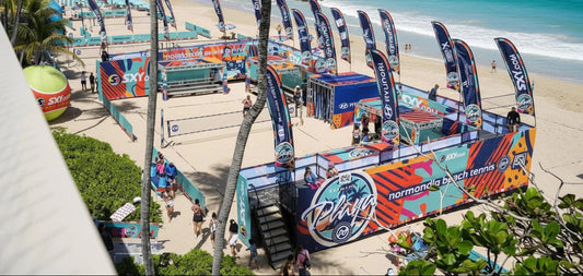 Aerial view of a branded beach tennis venue featuring sponsor feather flags, perimeter wraps, and courtside signage