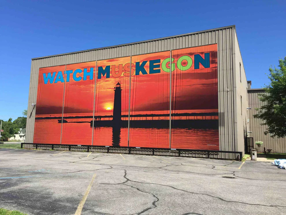 Full-wall custom building wrap featuring Watch Muskegon lighthouse artwork on a commercial facility exterior wall