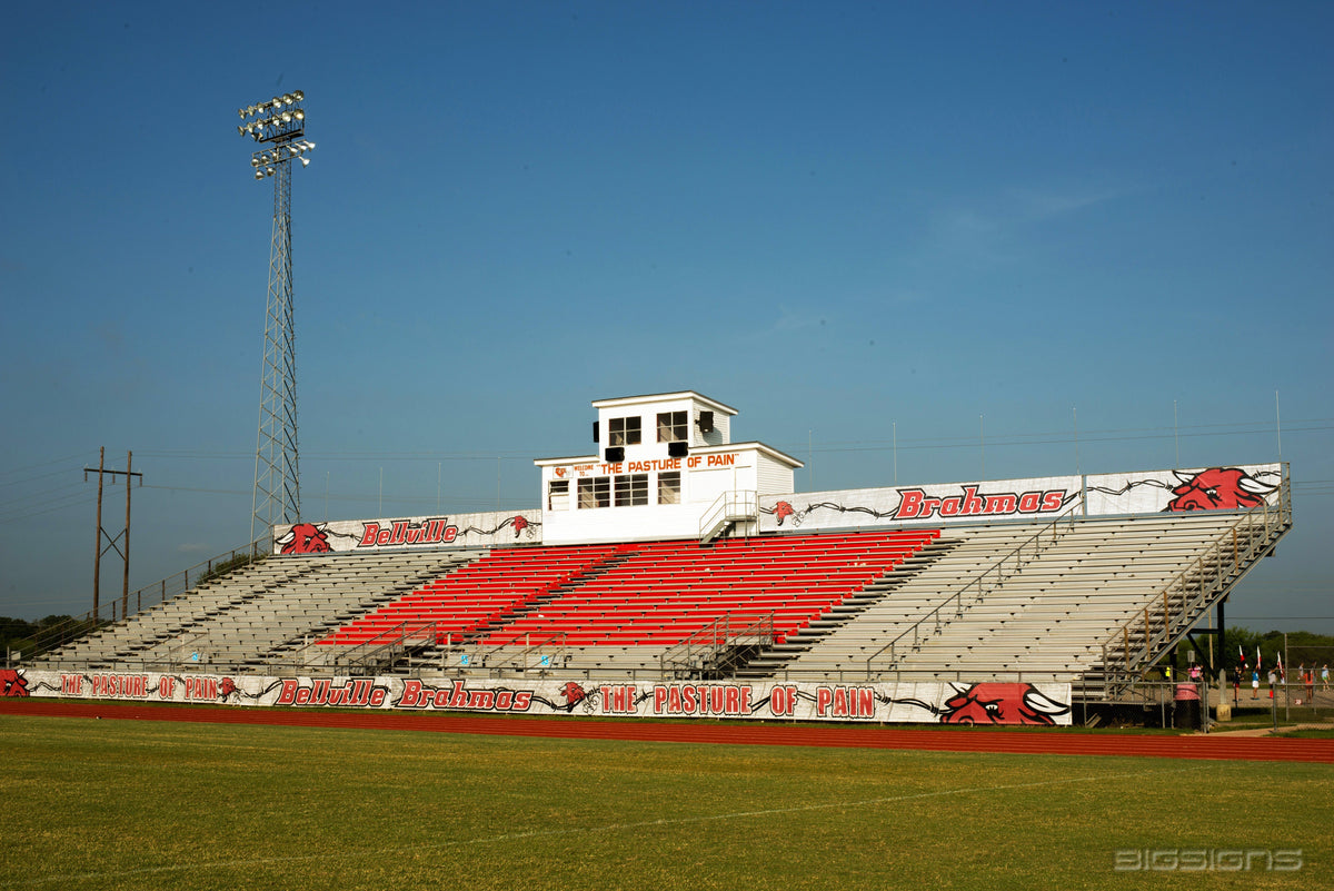 Football stadium grandstand with red and white Bellville Brahmas bleacher wraps and a Pasture of Pain fence wrap beside the track