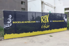 Black and yellow Rock la Cauze event fabric mesh banner on a fence