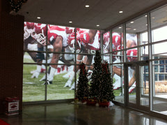 Custom-printed mesh windscreen on a black fence, displaying a lifelike image of a tree-filled forest and window.