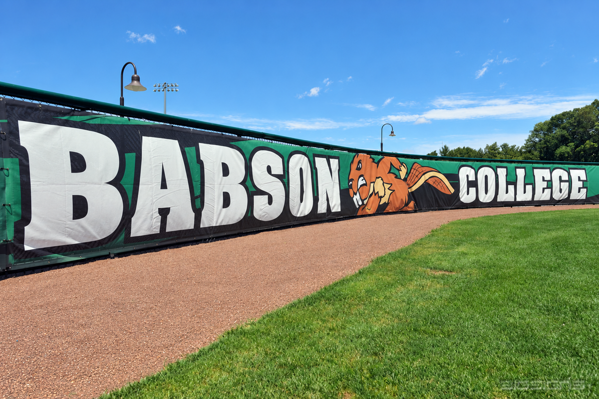 Green Babson College windscreen with beaver mascot on a baseball outfield fence