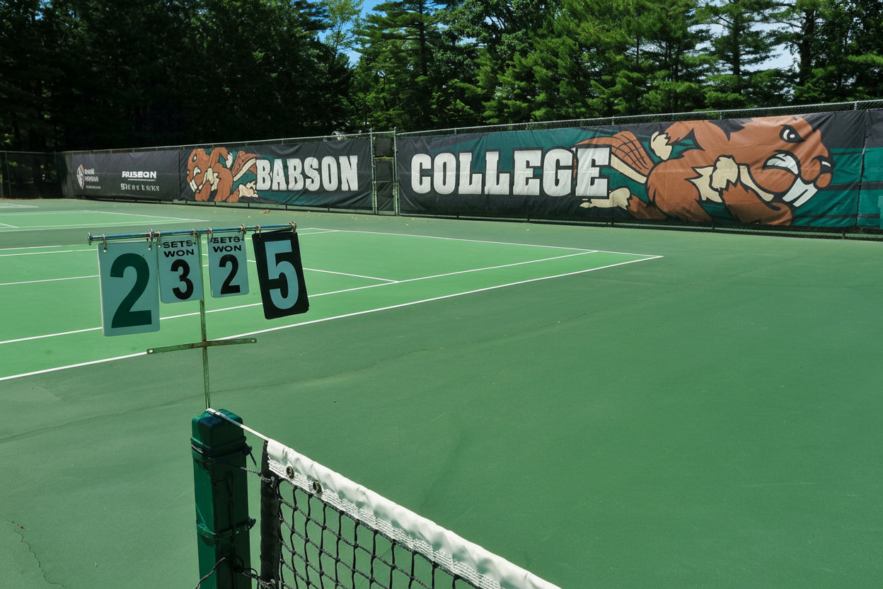 Mesh fence framing a quiet tennis court under daylight, creating a clean athletic scene with open space & a calm outdoor mood.