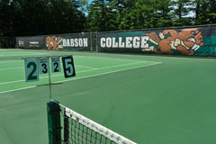 Mesh fence framing a quiet tennis court under daylight, creating a clean athletic scene with open space & a calm outdoor mood.