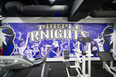 Purple-branded Bridgeport University weight room featuring professional power racks and a large wall mural with mascot.
