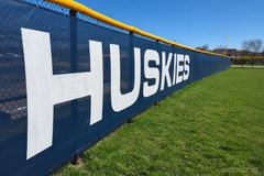 Navy Huskies windscreen with large white letters on an outfield fence