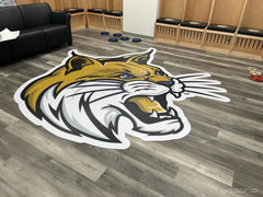 Gold and white wildcat head floor mat on a wood-look floor in a locker room lounge