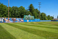Outfield wall windscreen with a baseball player mural beside a green scoreboard