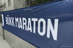Navy Bukk Maraton fabric mesh banner on a chain-link fence beside a building