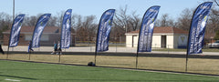 Outdoor promotional bow flag sign waving on flexible pole, attracting attention at sports or public events.