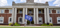 Runner carrying a blue flag on the lawn in front of a columned brick building, Hermann Hall