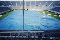 Blue tarp covering an entire football field under the goalposts in an empty stadium