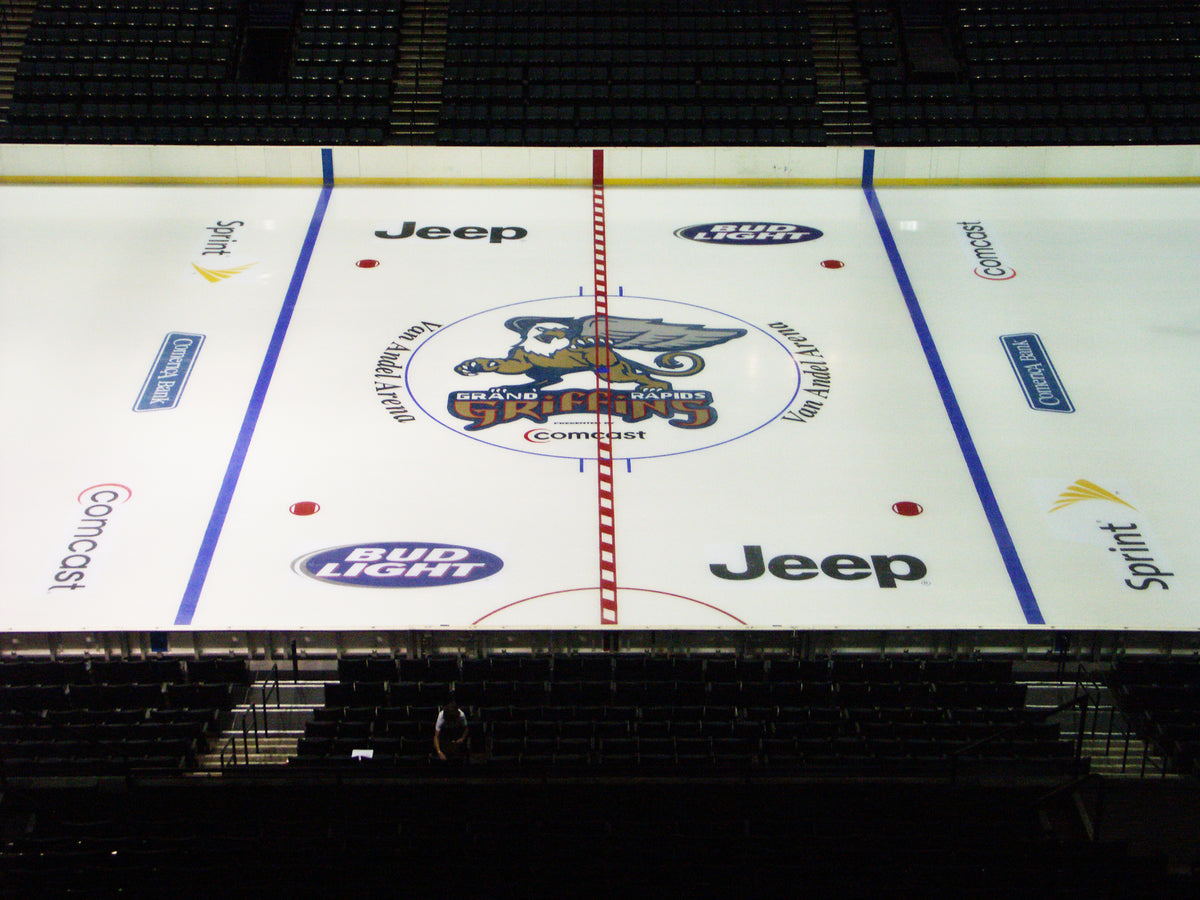 Center ice logos and sponsor graphics installed on a hockey rink featuring Grand Rapids branding and premium ad placement.
